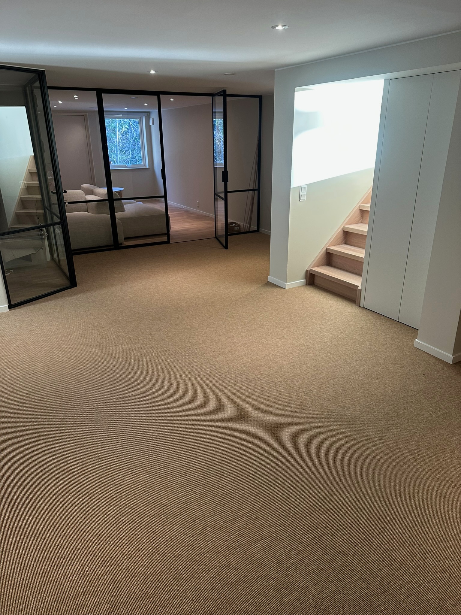 Källarvåning med sisalmatta, svart glasparti och trappa i ek